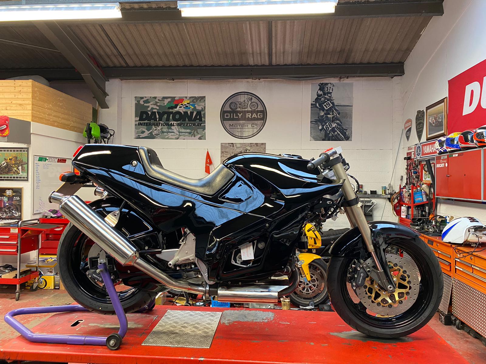 A black motorbike on the red lift in front of the workshop tool chests