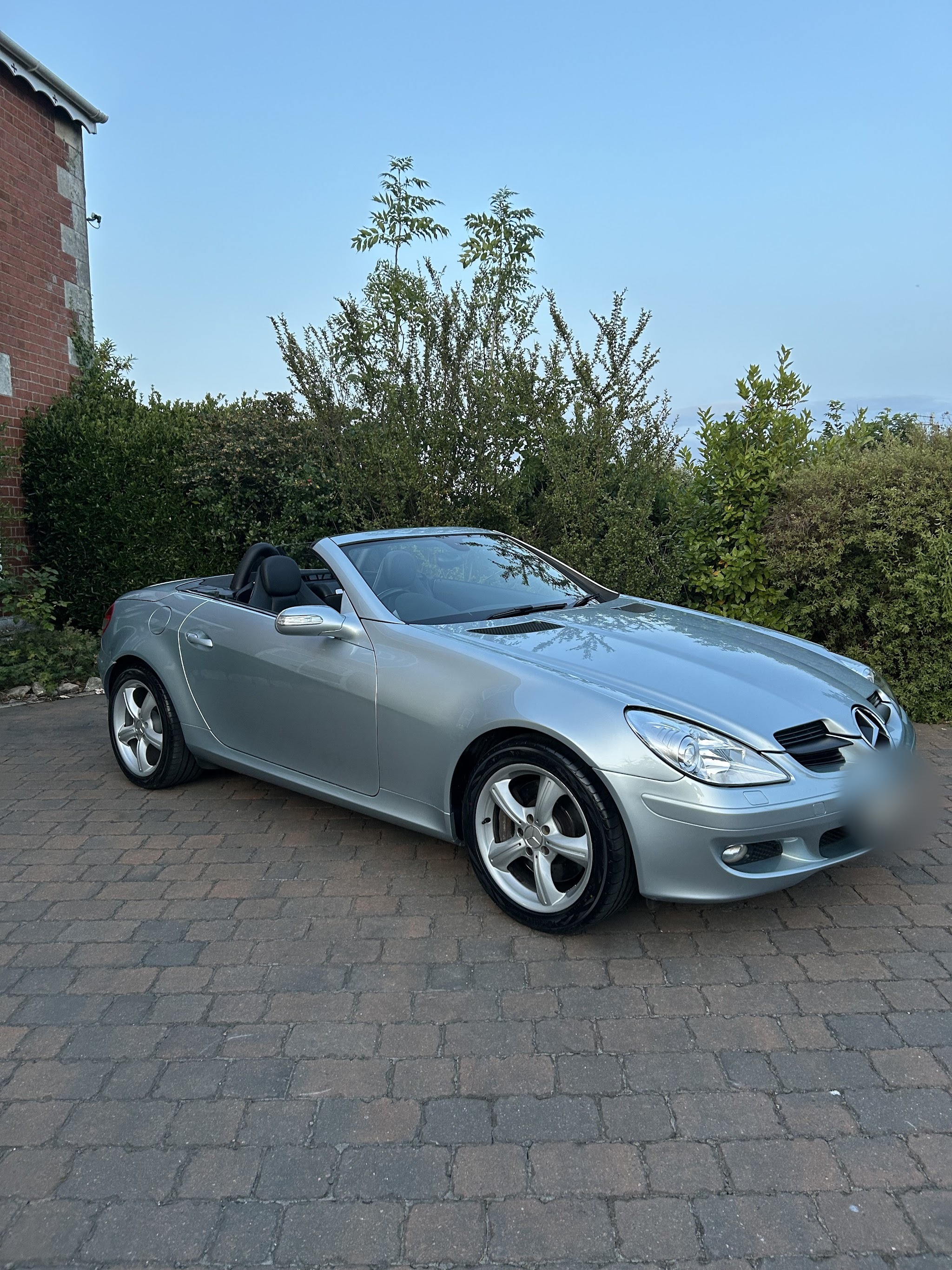 A silver Mercedes SLK convertible with the roof down on a block-paved drive